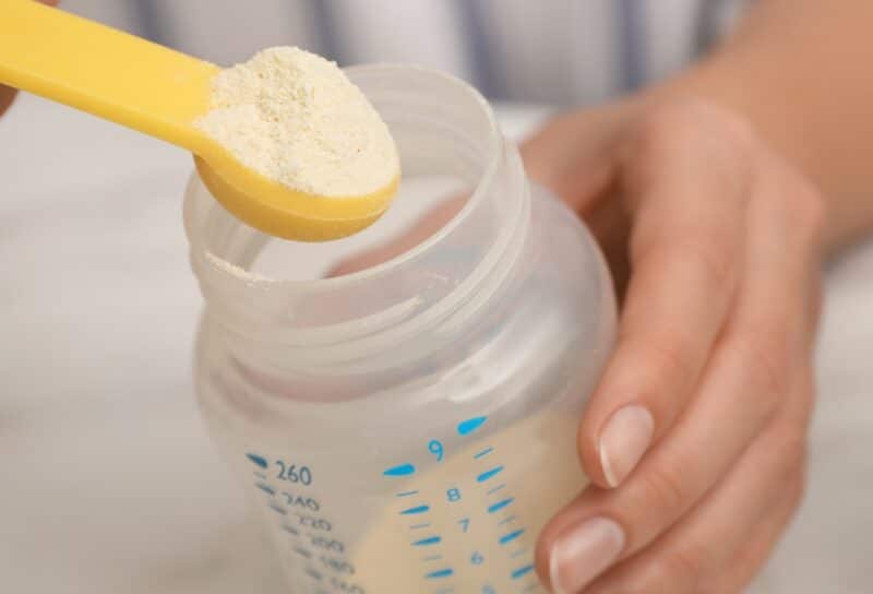 Woman preparing infant formula at table, closeup. Baby milk