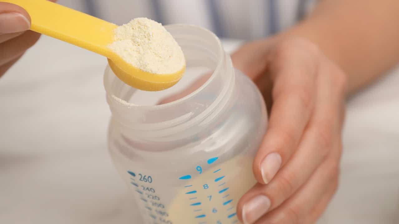 Woman preparing infant formula at table, closeup. Baby milk
