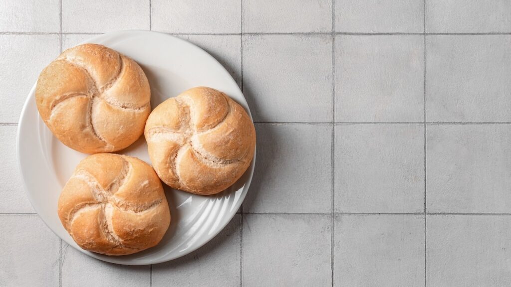 Plate with delicious kaiser rolls on grey tiled background