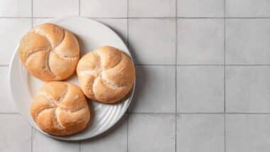 Plate with delicious kaiser rolls on grey tiled background