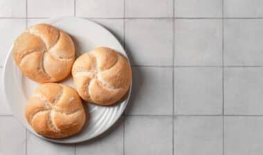 Plate with delicious kaiser rolls on grey tiled background