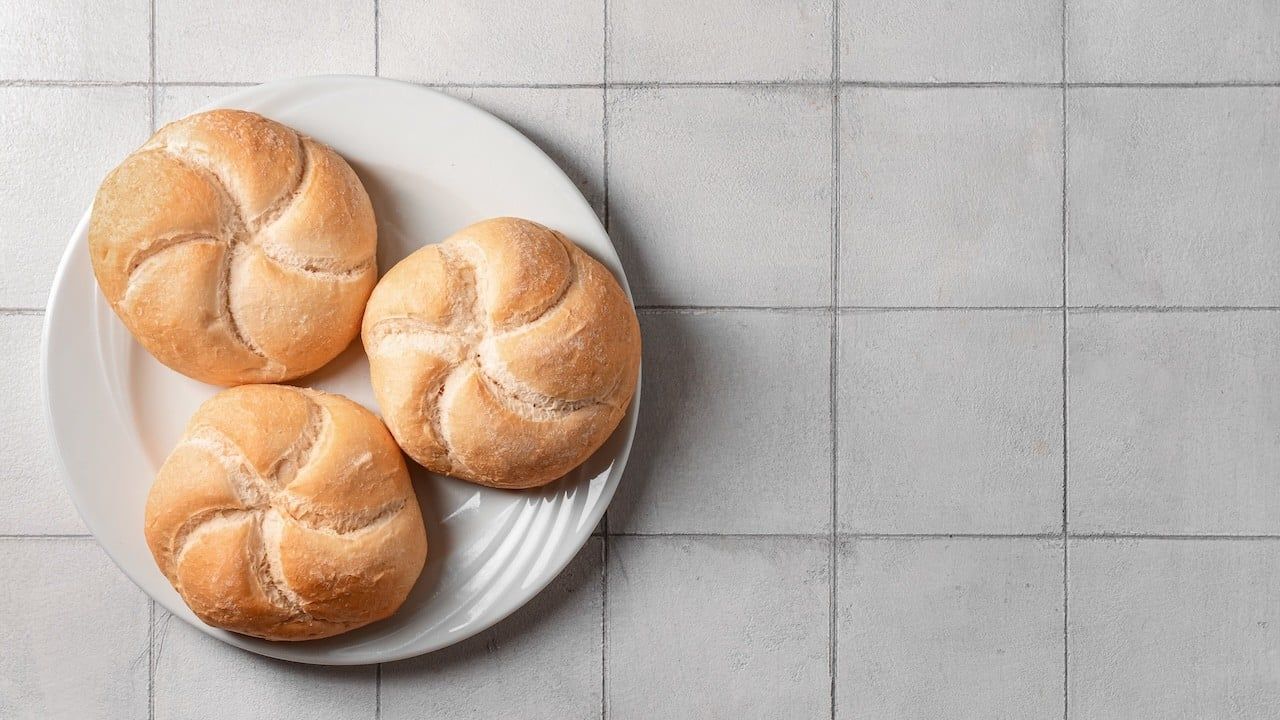 Plate with delicious kaiser rolls on grey tiled background