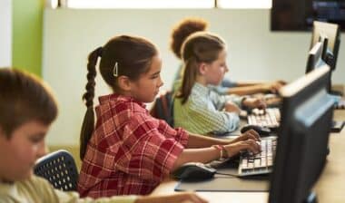 children sitting at desks using desktop computers in classroom