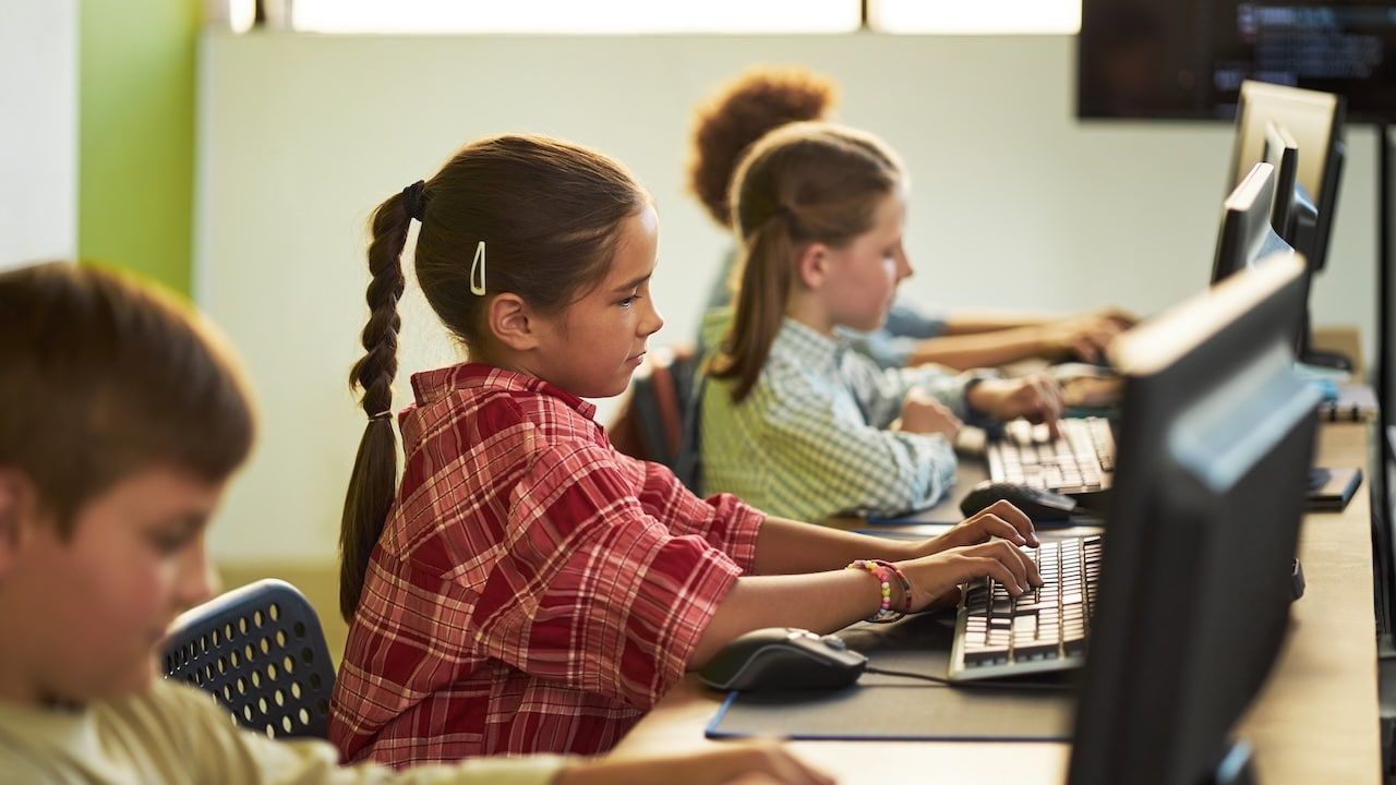 children sitting at desks using desktop computers in classroom