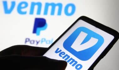 Venmo logo, a mobile payment service by Paypal, is displayed on a mobile phone screen and a monitor.