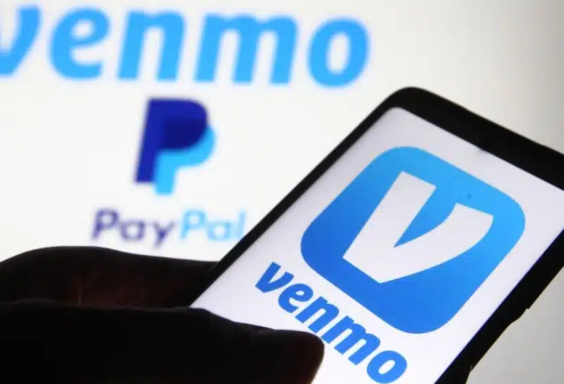 Venmo logo, a mobile payment service by Paypal, is displayed on a mobile phone screen and a monitor.