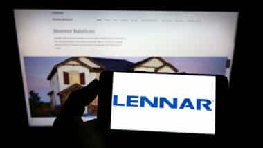 Person holding mobile phone with logo of US home construction company Lennar Corporation on screen in front of web page Focus on phone display
