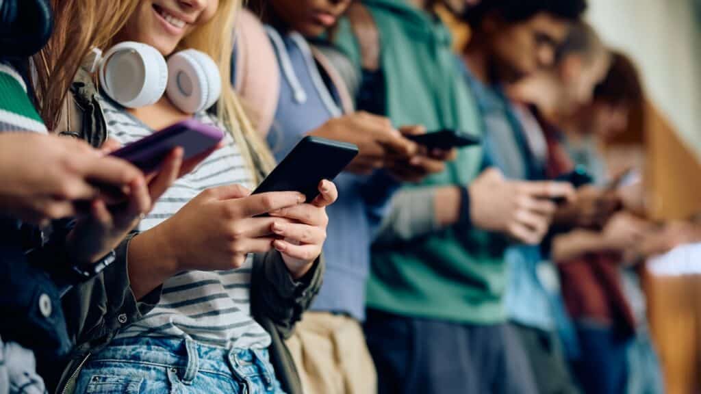Close up of teenage girl and her friends using mobile phones at high school hallway.