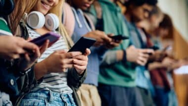 Close up of teenage girl and her friends using mobile phones at high school hallway.
