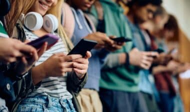 Close up of teenage girl and her friends using mobile phones at high school hallway.