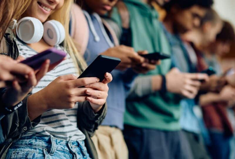 Close up of teenage girl and her friends using mobile phones at high school hallway.