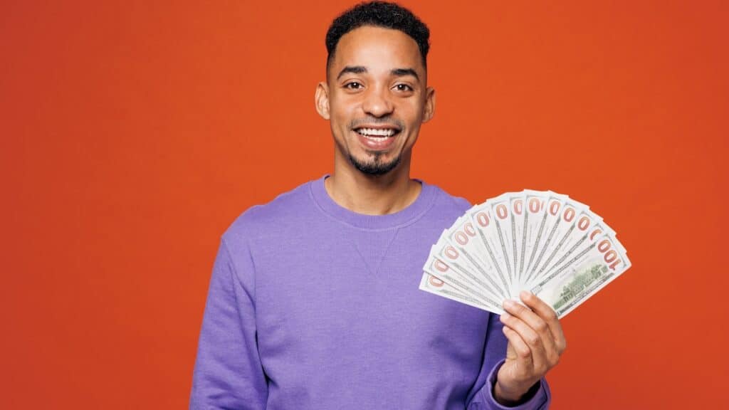 Young happy man wearing a purple sweatshirt holding cash money