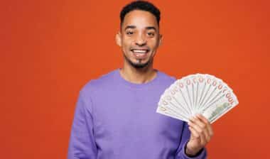 Young happy man wearing a purple sweatshirt holding cash money