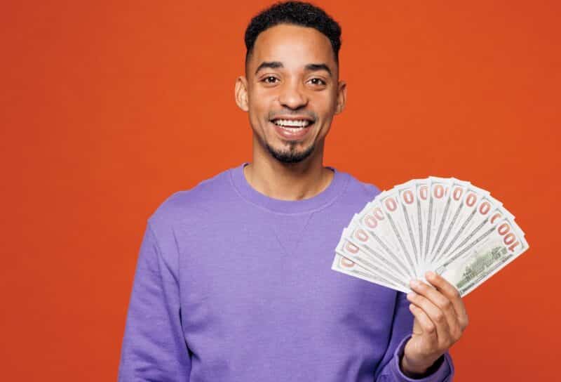 Young happy man wearing a purple sweatshirt holding cash money