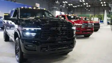 Black Ram pickup truck at 125th NY Auto Show Javits Center. Two red Ram trucks partially visible brightly lit large exhibition hall rugged design performance indoor display.