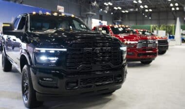 Black Ram pickup truck at 125th NY Auto Show Javits Center. Two red Ram trucks partially visible brightly lit large exhibition hall rugged design performance indoor display.