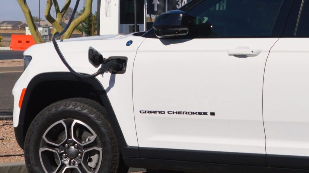White Jeep Grand Cherokee 4xe plug in hybrid SUV charging at an outdoor EV station.