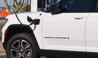 White Jeep Grand Cherokee 4xe plug in hybrid SUV charging at an outdoor EV station.