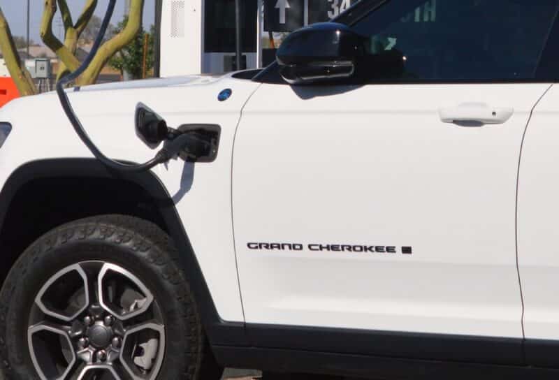 White Jeep Grand Cherokee 4xe plug in hybrid SUV charging at an outdoor EV station.