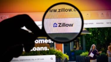 Closeup of a magnifying glass held over a computer screen displaying the zillow website homepage