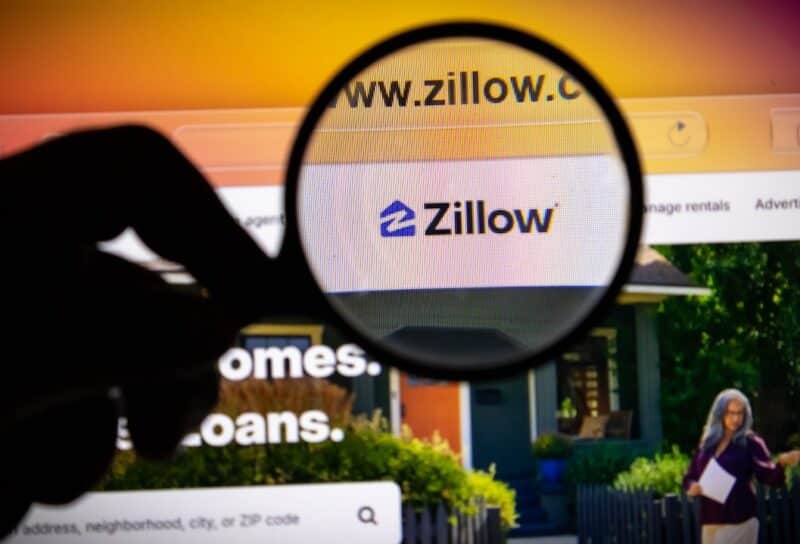 Closeup of a magnifying glass held over a computer screen displaying the zillow website homepage