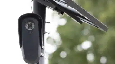 An AI Flock camera surveils a city street for car license plates.
