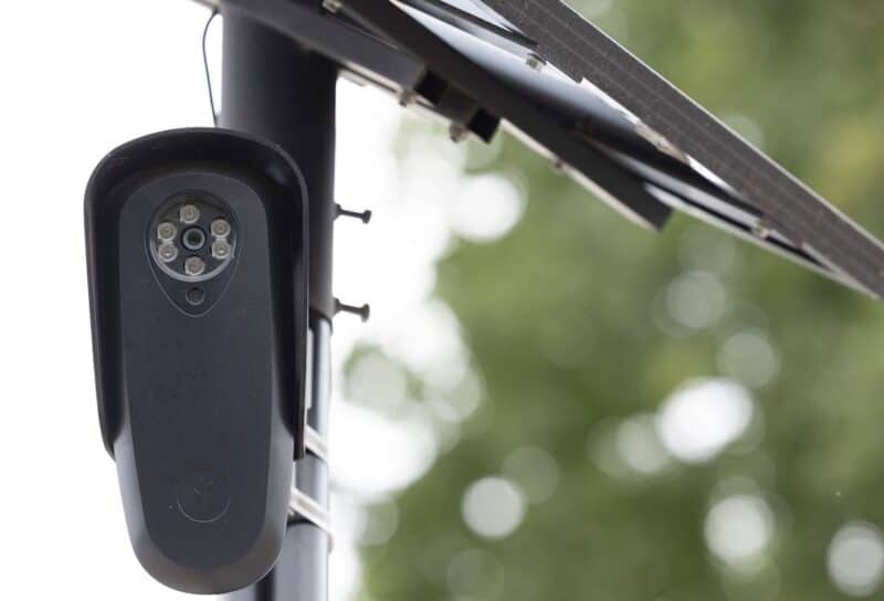 An AI Flock camera surveils a city street for car license plates.