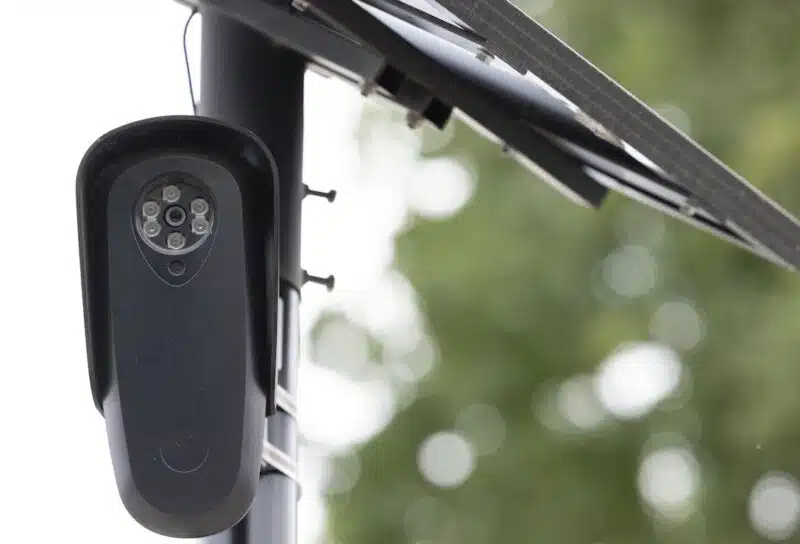 An AI Flock camera surveils a city street for car license plates.