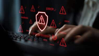 Hands Typing on Keyboard with Digital Security Warnings and Alerts Displayed on Screen Representing Cybersecurity Risks and Data Protection Issues