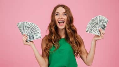 Portrait of a happy excited woman with long hair holding bunch of money banknotes in each hand