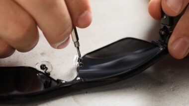 Handyman repairing sunglasses with screwdriver at grey table, closeup