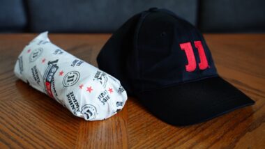 Sub sandwich wrapped in Jimmy John's food paper wrap sits on the table with employee hat.
