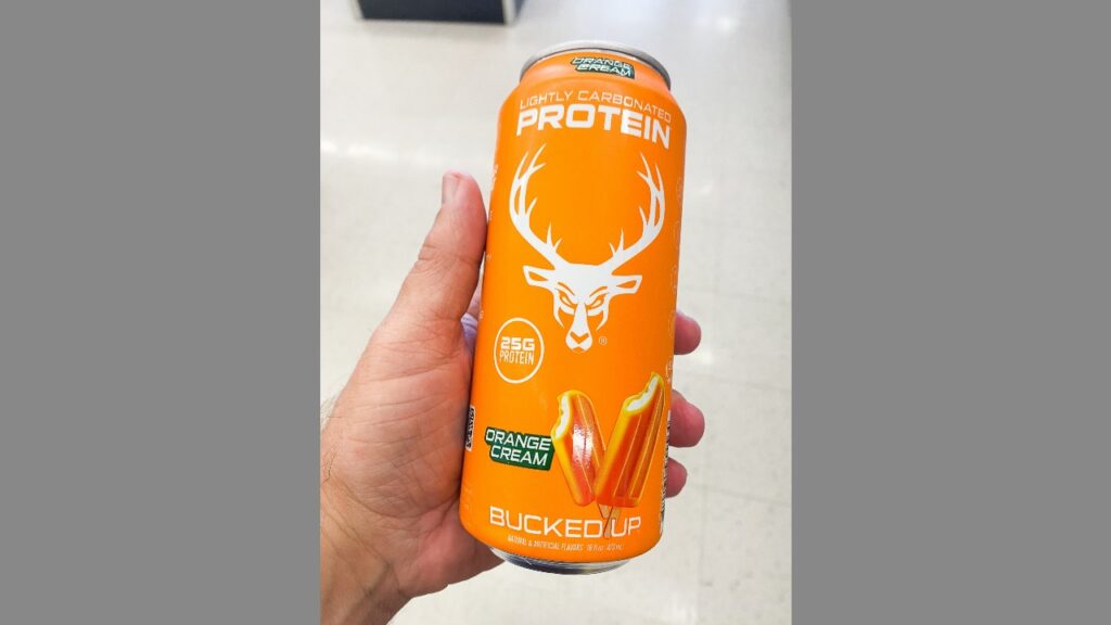 Hand holding an orange can of Bucked Up lightly carbonated protein drink orange cream flavor