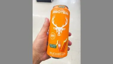 Hand holding an orange can of Bucked Up lightly carbonated protein drink orange cream flavor