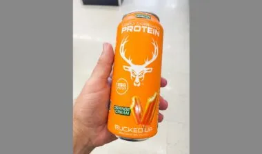 Hand holding an orange can of Bucked Up lightly carbonated protein drink orange cream flavor