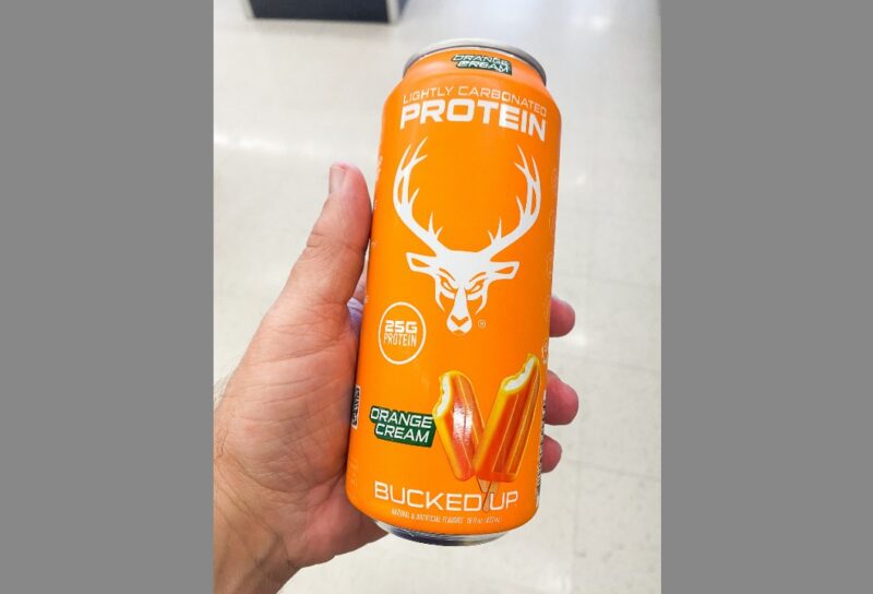 Hand holding an orange can of Bucked Up lightly carbonated protein drink orange cream flavor