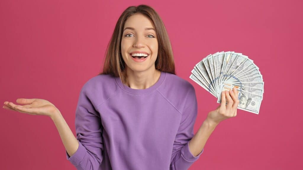 Happy young woman with cash money on pink background