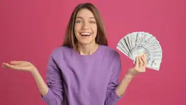 Happy young woman with cash money on pink background