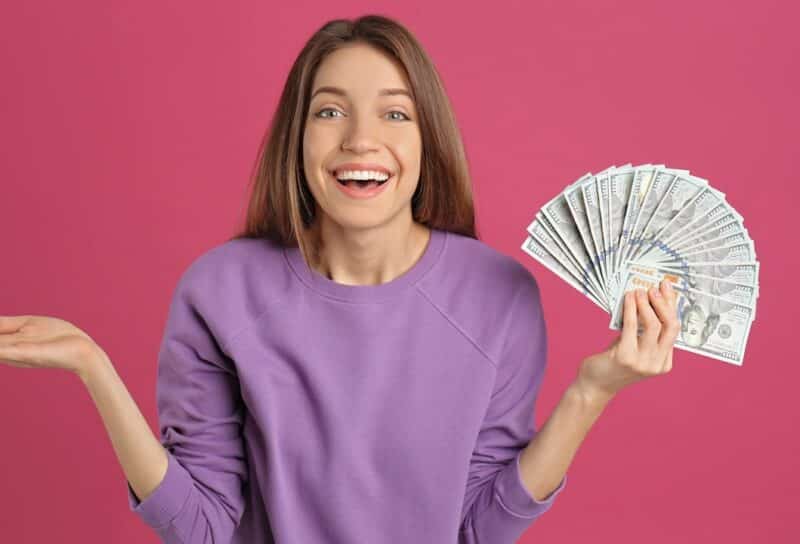 Happy young woman with cash money on pink background