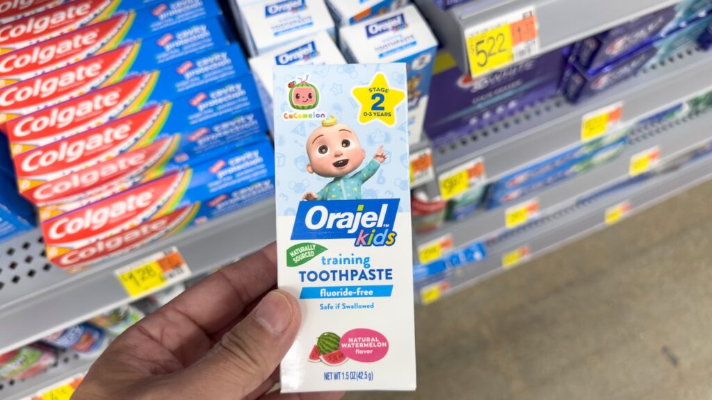 A view of a hand holding a package of Orajel Kids toothpaste, on display at a local retail store.