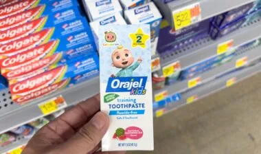 A view of a hand holding a package of Orajel Kids toothpaste, on display at a local retail store.