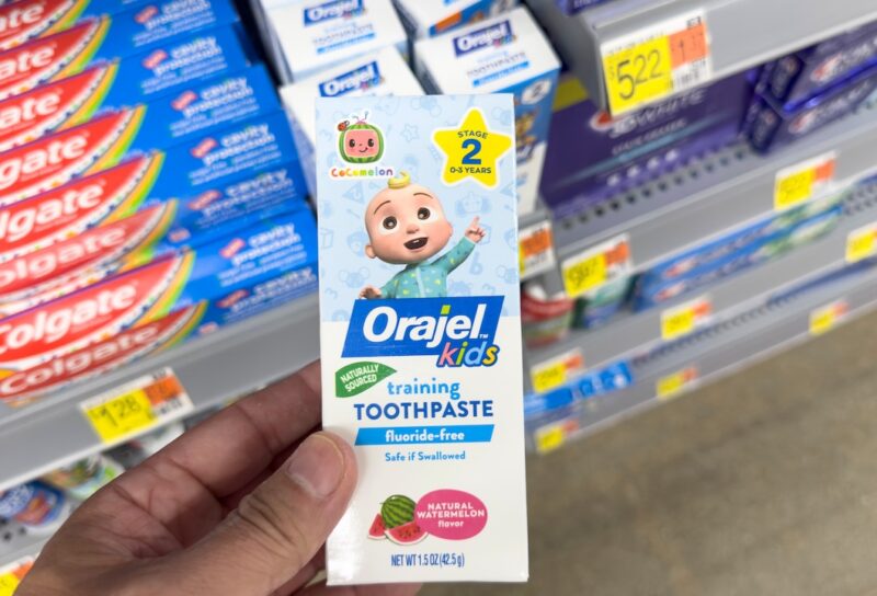 A view of a hand holding a package of Orajel Kids toothpaste, on display at a local retail store.