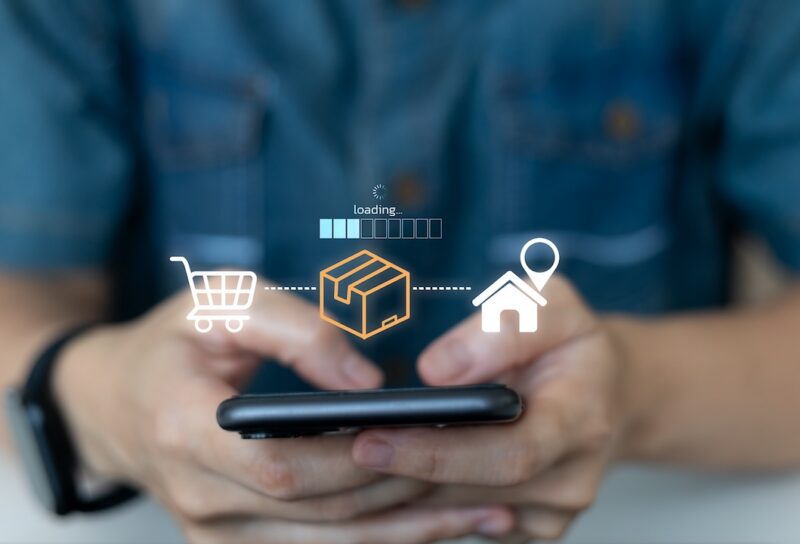 Close-up of hands holding smartphone with icons showing online shopping, package shipping, and home delivery process. Concept of e-commerce logistics and real-time delivery tracking.