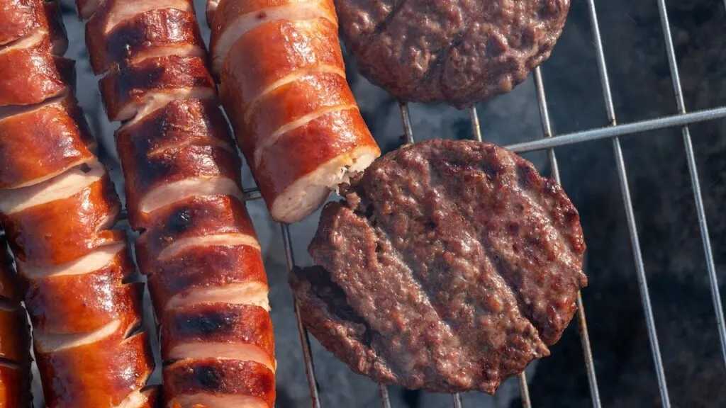 beef burgers and grilled sausages cooking on a barbecue grill outdoors