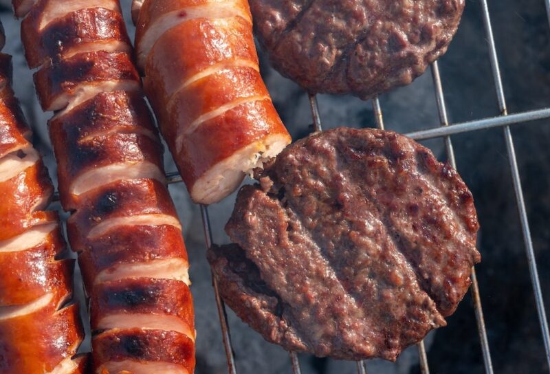 beef burgers and grilled sausages cooking on a barbecue grill outdoors