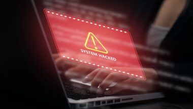 Business professional using a laptop with red system hacked warning interface