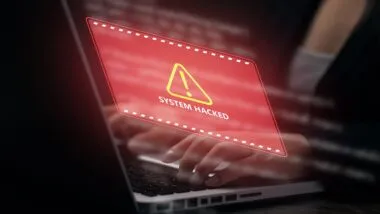 Business professional using a laptop with red system hacked warning interface