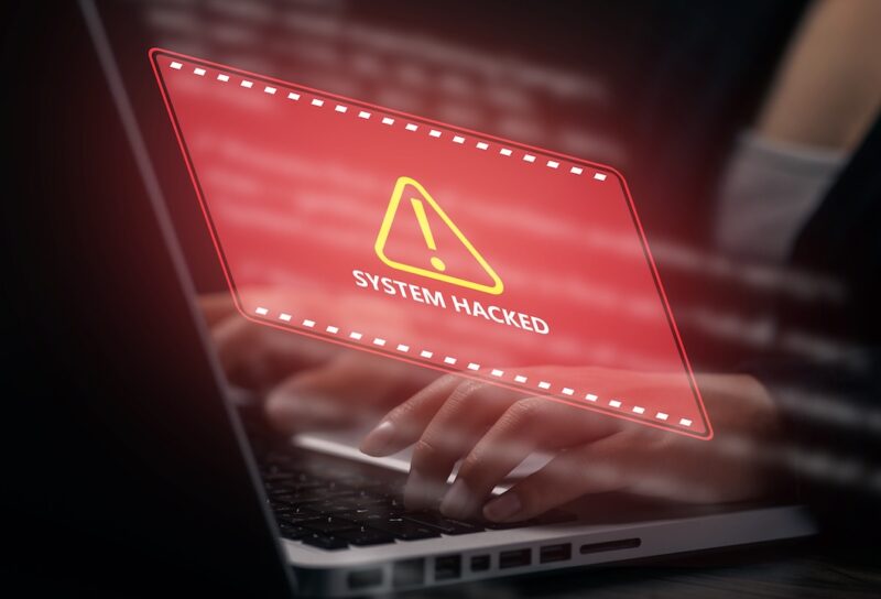 Business professional using a laptop with red system hacked warning interface