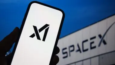 xAI logo displayed on a smartphone with SpaceX branding visible on a screen in the background