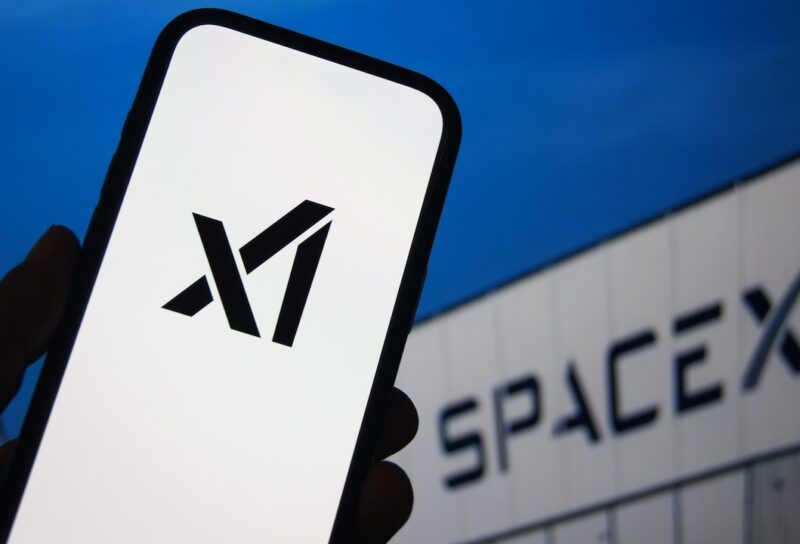 xAI logo displayed on a smartphone with SpaceX branding visible on a screen in the background